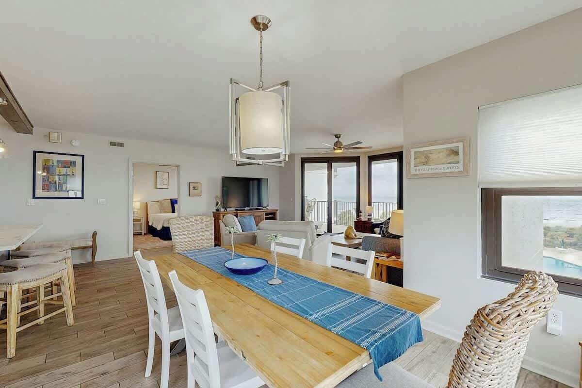 A spacious dining area with a wooden table, white chairs, and a blue table runner.