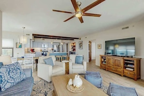 A modern living room with a ceiling fan, a TV, and a dining area with chairs and a table. - Palmetto Sunrise Waterfront Condo (Litchfield Beach)