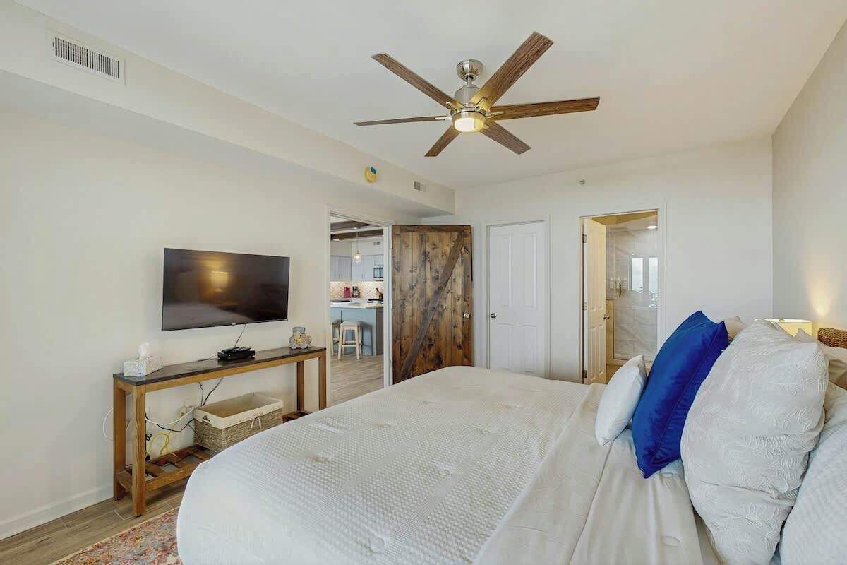 Ein Schlafzimmer mit einem Bett, einem Deckenventilator, einem Fernseher und einer Holztür.