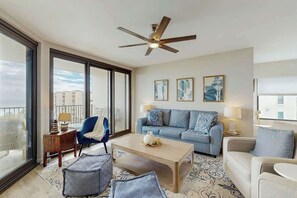 Ein geräumiges Wohnzimmer mit großem Fenster, Deckenventilator, einer Sofagarnitur und einem Couchtisch.