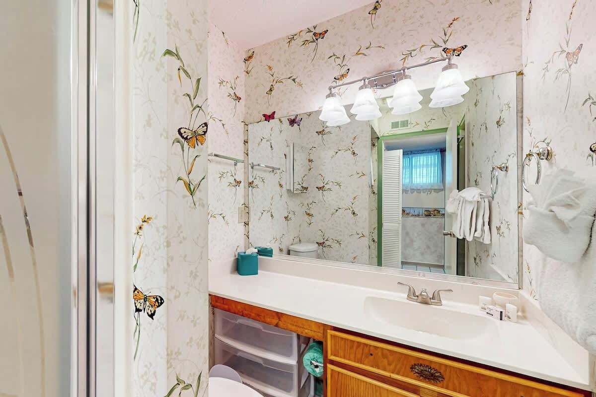 A bathroom with floral wallpaper, a mirror, a sink, and a shower area.