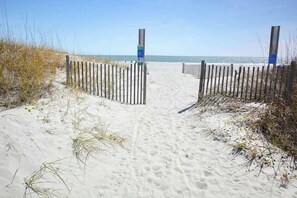 Ein sandiger Küstenpfad führt zum Meer, gesäumt von Holzzäunen.