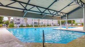 An indoor swimming pool with a covered roof, surrounded by a fence, and adjacent to residential buildings. - Arcadian Dunes 19-374 (Myrtle Beach)
