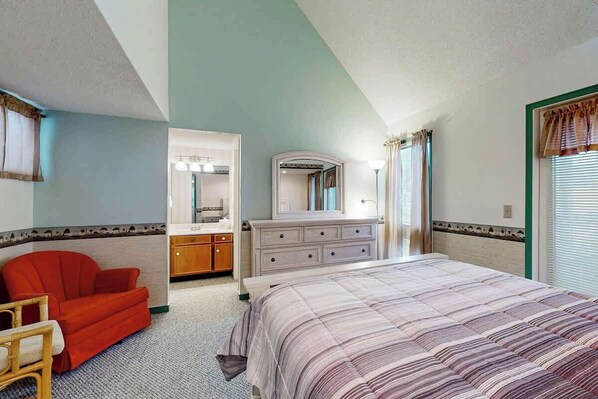 Een slaapkamer met een bed, een rode stoel, een kaptafel en een spiegel.