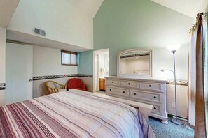 Een slaapkamer met een bed, een dressoir, een stoel, een spiegel en een vloerlamp.