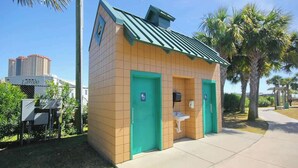 A small, single-story building with a green roof and two doors, one of which has a wheelchair symbol. - Arcadian Dunes 19-374 (Myrtle Beach)