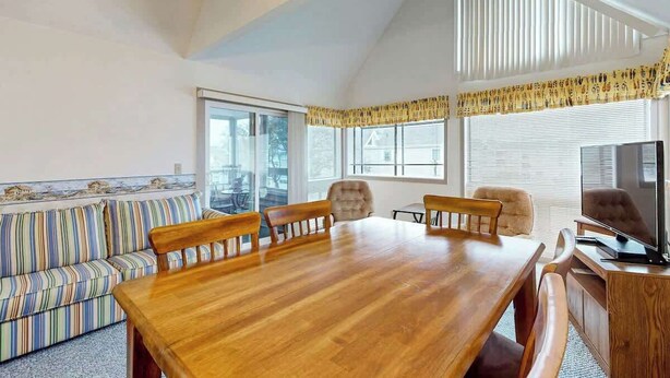 A dining area with a wooden table and chairs, a sofa, and a television. - Arcadian Dunes 19-374 (Myrtle Beach)