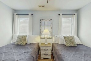 A room with two beds, a nightstand with drawers, a lamp, and a window with curtains. - Dry Dock Condo Unit 204 (Myrtle Beach)