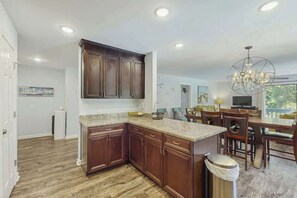 A modern kitchen with dark wood cabinets, granite countertops, and a dining area with a chandelier. - Dry Dock Condo Unit 204 (Myrtle Beach)