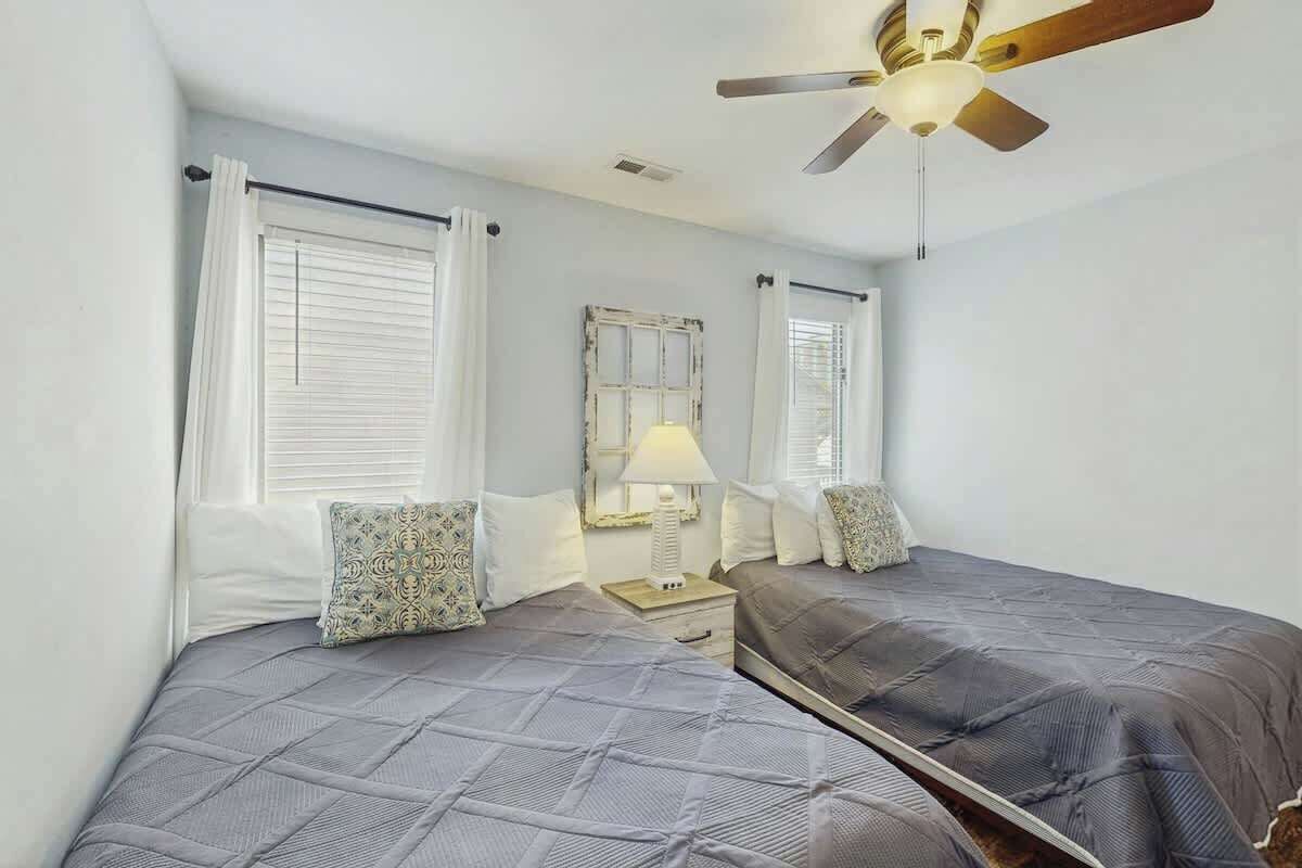 A twin bedroom with two beds, a ceiling fan, a nightstand with a lamp, and a mirror.