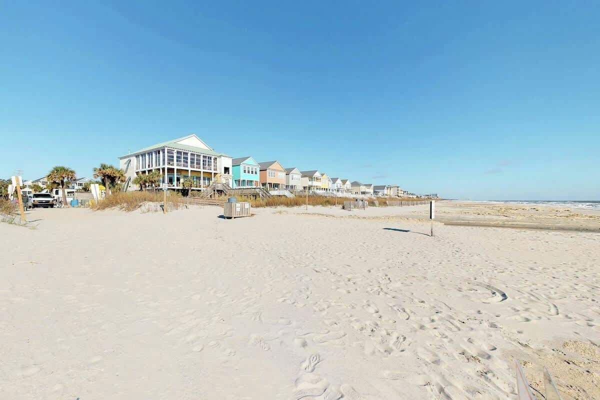 A beachside hotel with a row of beach houses, a sandy beach, and a clear sky.
