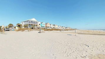 A beachside hotel with a row of beach houses, a sandy beach, and a clear sky.