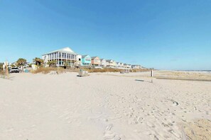 Un hotel frente a la playa con una hilera de casas, una playa arenosa y un cielo despejado.