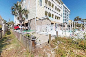 A multi-story building with balconies, a swimming pool, and a wooden fence. - Ocean Views at The Beach (North Myrtle Beach)