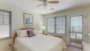 Ein Schlafzimmer mit einem Bett, einem Deckenventilator, einem Fenster mit Jalousien und einer Tür mit Blick.