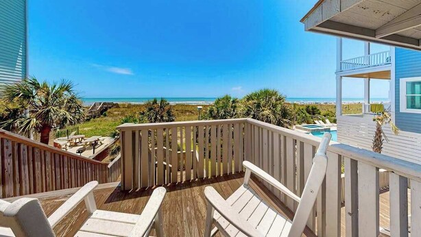 A wooden deck with white chairs overlooking a beach.