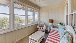 A room with large windows, a wicker chair, a small table, and a sofa with striped cushions.