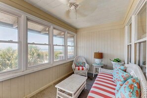 A room with large windows, a wicker chair, a small table, and a sofa with striped cushions.