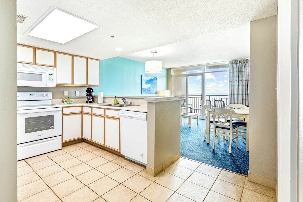 A modern kitchen with white appliances, a blue accent wall, and a view of a balcony with a dining area.