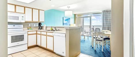 Una cocina moderna con electrodomésticos blancos, una pared de acento azul y vistas a un balcón con zona de comedor.