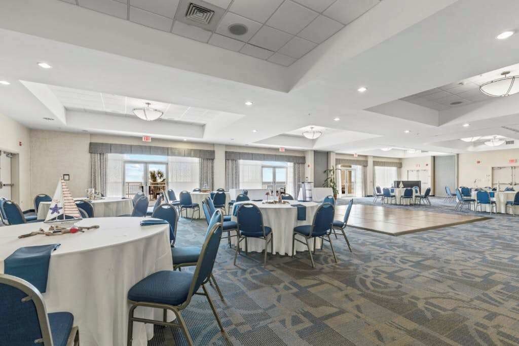 Un salón de conferencias de hotel con mesas redondas, sillas y un amplio piso alfombrado.