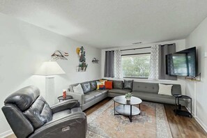 A modern living room with a sectional sofa, a coffee table, and a flat-screen TV mounted on the wall. - Sea Turtle Ocean View Condo (Myrtle Beach)