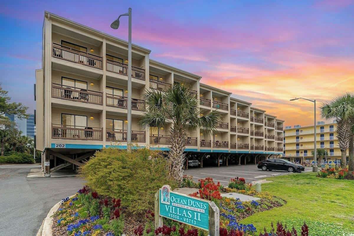A multi-story hotel with balconies, a sign indicating 'Ocean Dunes Villas,' and a parking area.