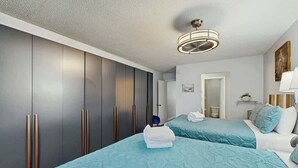 Een hotelkamer met twee bedden, een kledingkast, een plafondlamp en een deur naar een andere kamer.