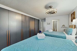 Ein Hotelzimmer mit zwei Betten, einem Kleiderschrank, einer Deckenleuchte und einer Tür zu einem weiteren Raum.