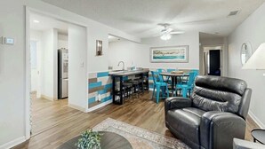 Een moderne woonkamer met een leren bank, een eetgedeelte met blauwe stoelen, en een keuken met een koelkast.
