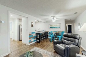 Ein modernes Wohnzimmer mit einer Ledersofa, einem Essbereich mit blauen Stühlen und einer Küche mit einem Kühlschrank.