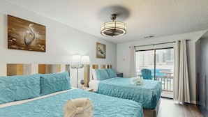 Hotelkamer met twee bedden, een plafondventilator, kunstwerken aan de muren en uitzicht op de stad.
