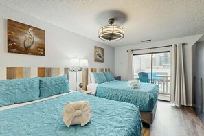 Ein Hotelzimmer mit zwei Betten, einem Deckenventilator, Kunstwerken an den Wänden und Blick auf die Stadt durch das Fenster.