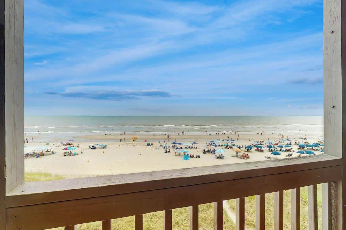 A beach view from a wooden balcony with a railing.