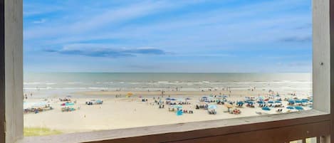 A beach view from a wooden balcony with a railing.