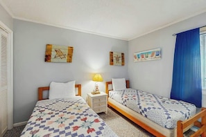 A room with two beds, a nightstand with a lamp, and wall art. - Atlantic Escape Oceanfront Condo (North Myrtle Beach)