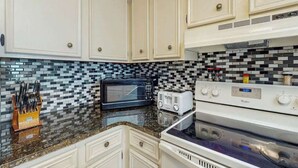 A kitchen with white cabinets, a microwave, a toaster, and a stove. - Atlantic Escape Oceanfront Condo (North Myrtle Beach)