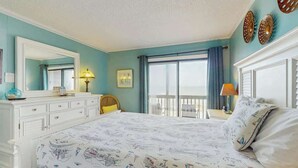 A bedroom with a large bed, a dresser, a window with a view, and decorative wall art. - Atlantic Escape Oceanfront Condo (North Myrtle Beach)