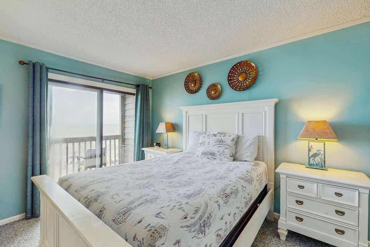 Une chambre avec un grand lit, deux tables de chevet, une fenêtre avec des rideaux et des œuvres d’art décoratives au mur.