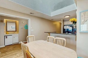 A compact kitchen with a dining area, featuring a small refrigerator, a sink, and a dining table with four chairs. - Atlantic Escape Oceanfront Condo (North Myrtle Beach)