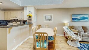 A modern kitchen with white cabinets, a dining table with chairs, and a sofa with a patterned cushion. - Atlantic Escape Oceanfront Condo (North Myrtle Beach)