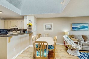 Eine moderne Küche mit weißen Schränken, einem Esstisch mit Stühlen und einem Sofa mit einem gemusterten Kissen.
