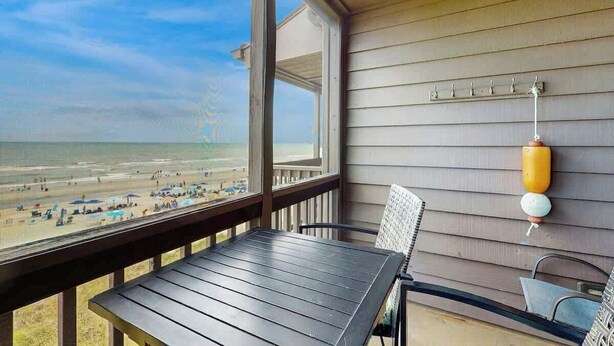 A balcony with a view of the beach, a table, chairs, and a wall-mounted hook. - Atlantic Escape Oceanfront Condo (North Myrtle Beach)