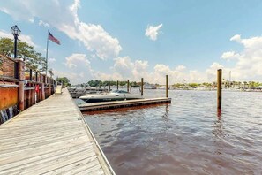 Eine hölzerne Steg ragt in ruhiges Wasser, wo Boote festgemacht sind, ein klarer Himmel und eine amerikanische Flagge sind zu sehen.