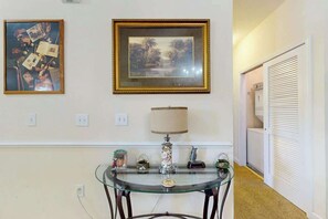 Une pièce avec une table en verre, une lampe et deux tableaux encadrés accrochés au mur.