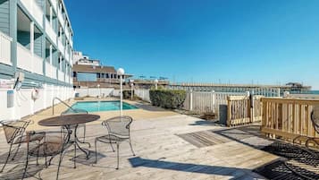 A pool area with a wooden deck, metal chairs, and a view of the pier.