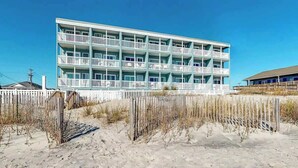 A multi-story hotel with balconies, located near a sandy beach. - Beachfront Blessing Oceanfront Condo (Garden City Beach)