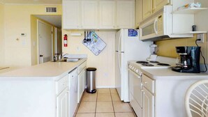 A compact kitchen with white cabinets, a microwave, a stove, and a coffee maker. - Beachfront Blessing Oceanfront Condo (Garden City Beach)