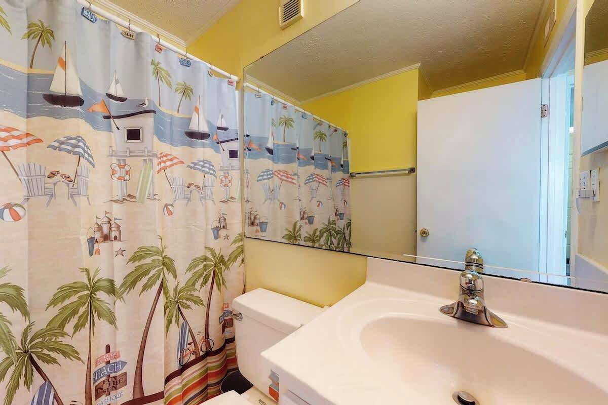 Une salle de bain avec un lavabo blanc, des toilettes et un rideau de douche à motifs de plage.