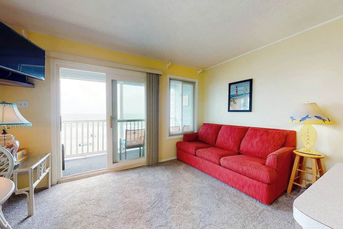 Une pièce avec un canapé rouge, une petite table, une chaise, une lampe et un tableau au mur.